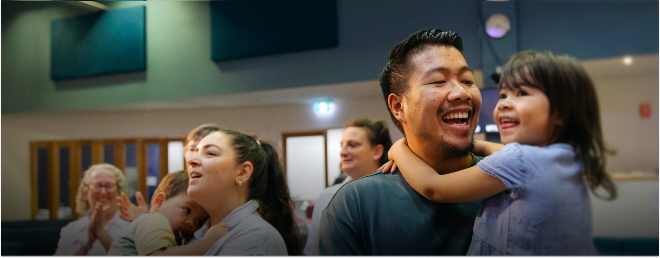 Two parents hold their young children as they all sing during a Sunday service.