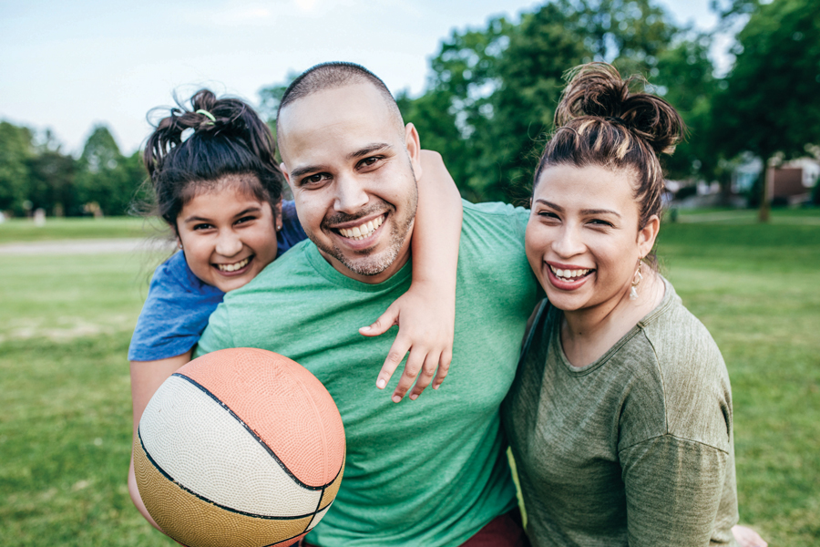 A couple with a child at a park holding a basketball