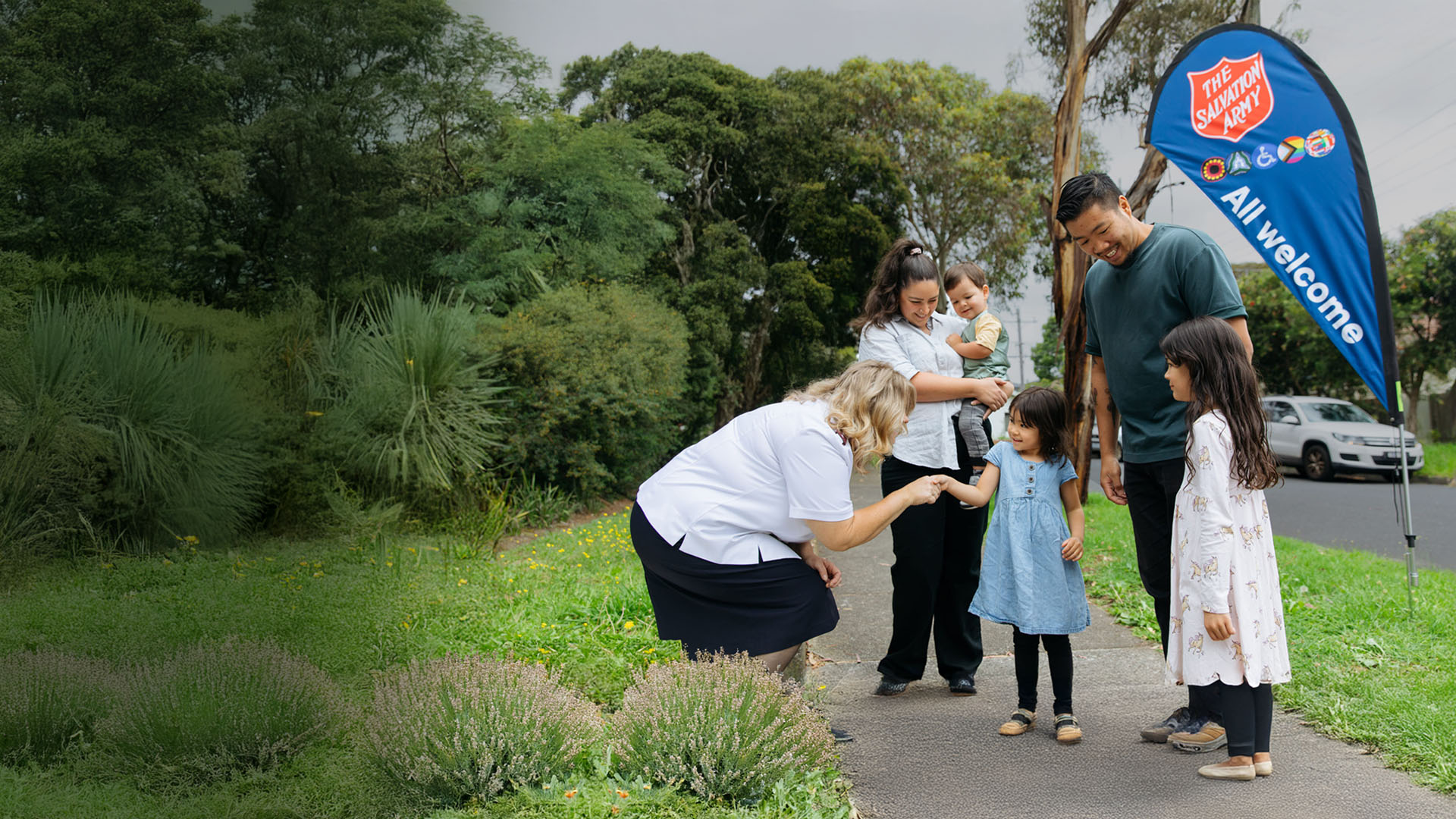 A Salvation Army officer warmly greeting a family of five on a path.