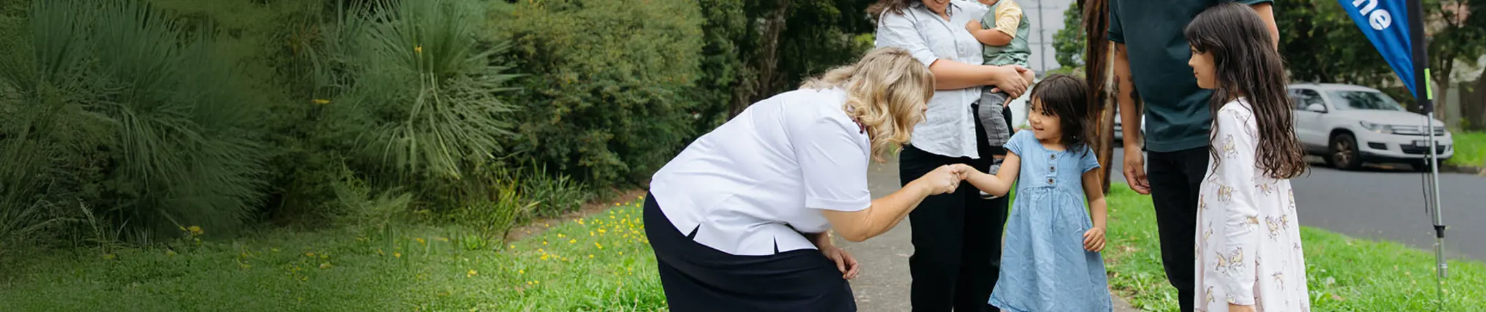 A Salvation Army officer warmly greeting a family of five on a path.