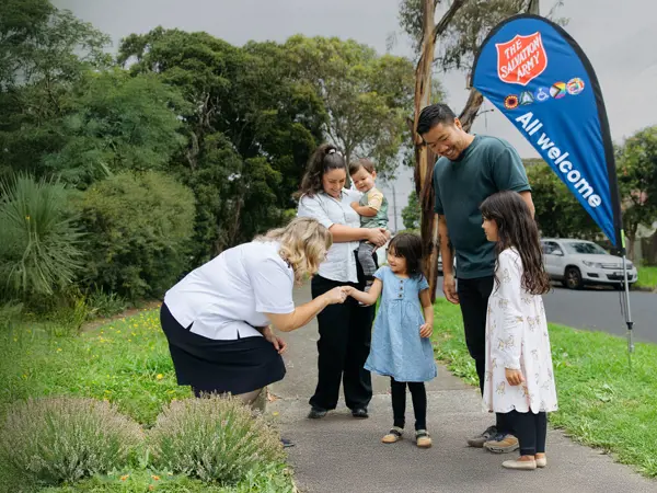 A Salvation Army officer warmly greeting a family of five on a path.