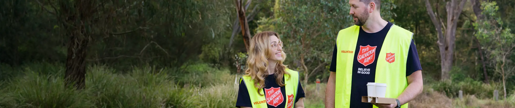 Two Salvation Army volunteers sharing a friendly conversation in a park, ready with warm coffee, blankets, and open hearts to support those doing it tough.