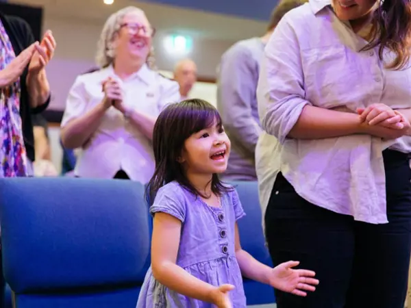 A young girl sings and claps enthusiastically during a church service with her family.