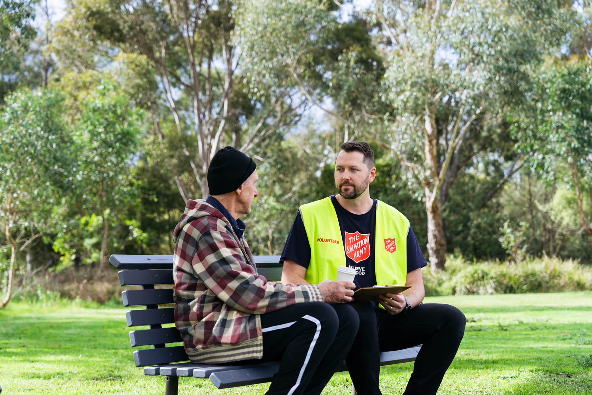 A Salvos volunteer listens to an older man tell his story on a park bench.