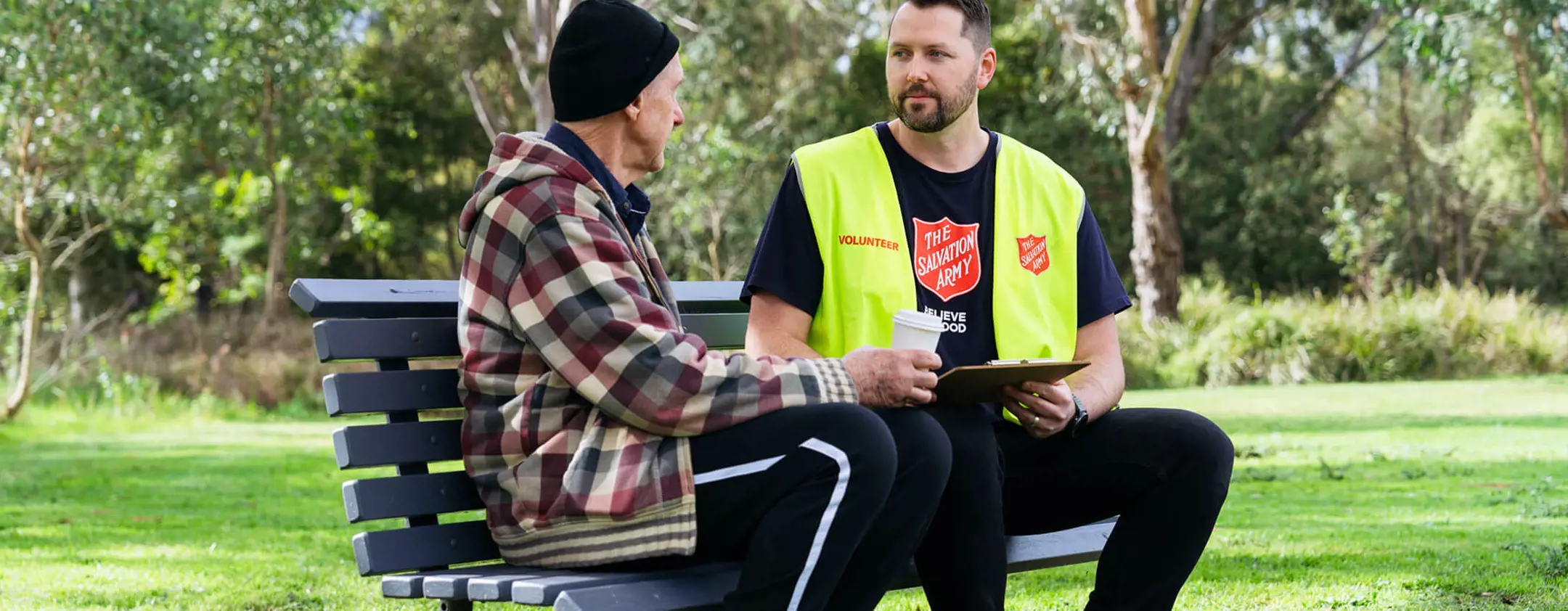 A Salvos volunteer listens to an older man tell his story on a park bench.