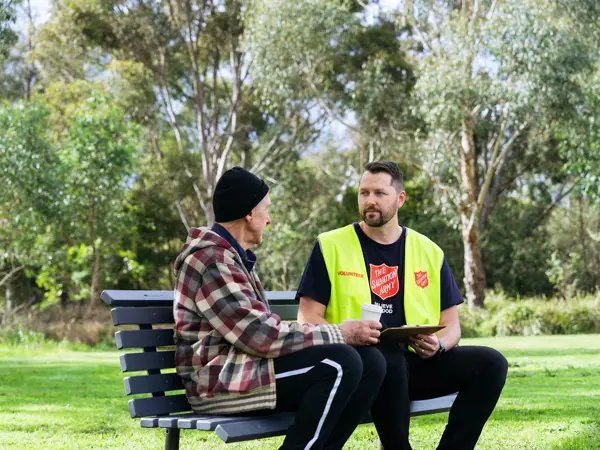 A Salvos volunteer listens to an older man tell his story on a park bench.