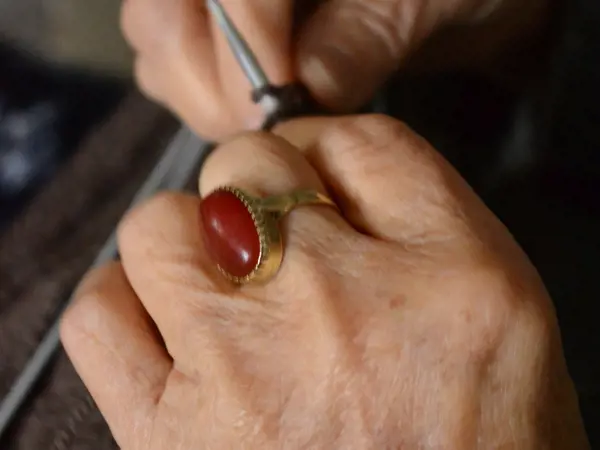 Person knitting with a ruby ring on their finger.