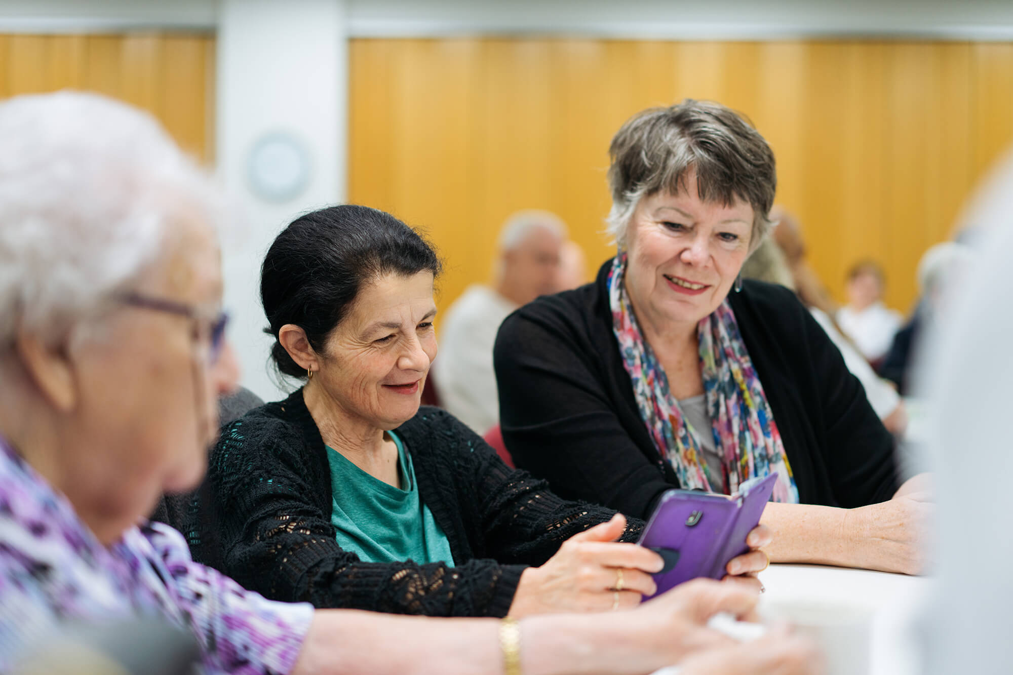 A diverse group of older community members enjoying fellowship and share photos on their phones..