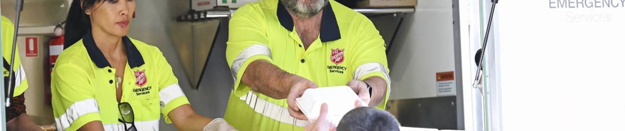 Two Salvation Army Emergency Services workers serve food and drink from the Food Truck window