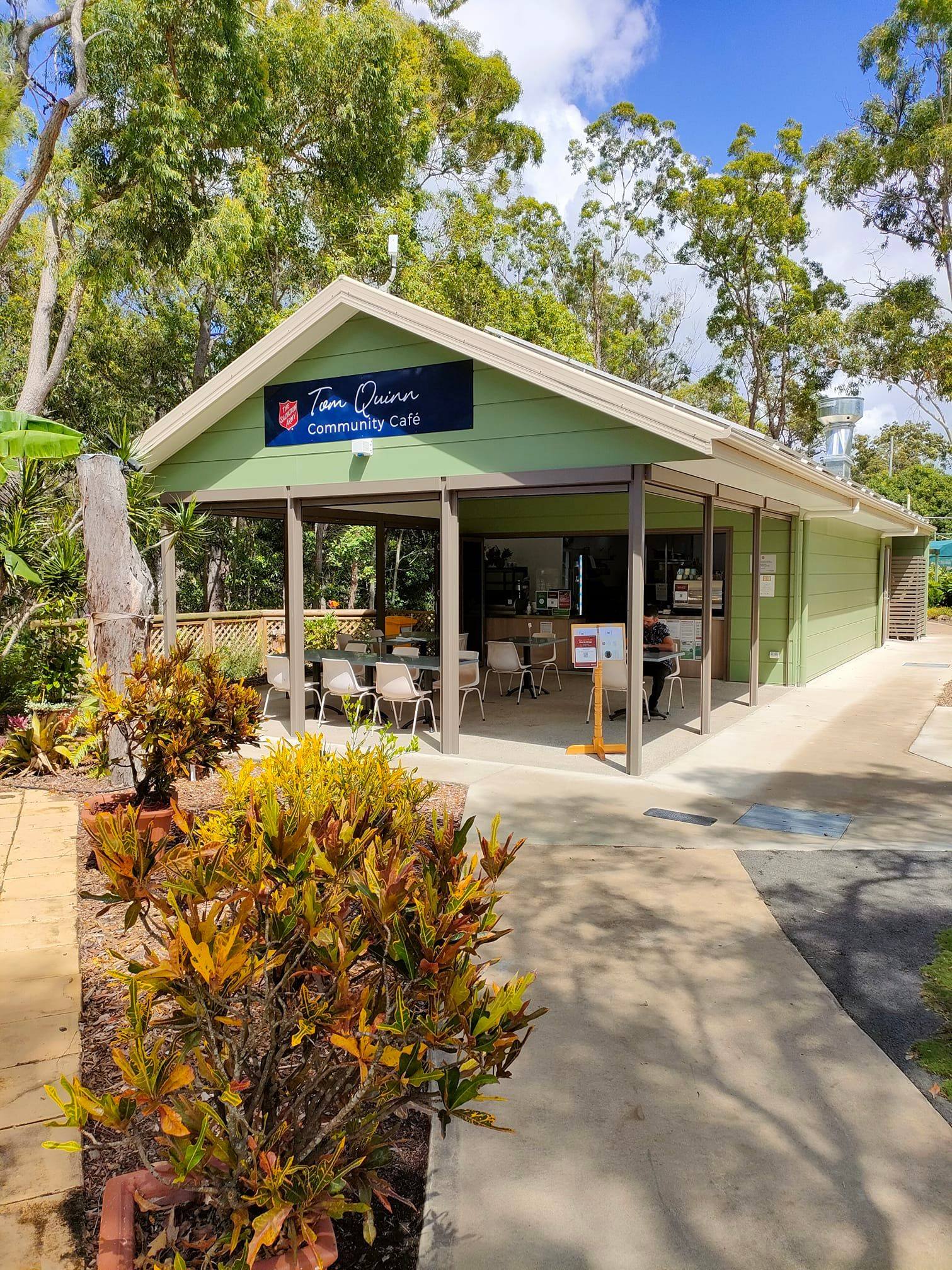 The Tom Quinn Community Cafe - a light green, pitch-roofed cabin with a shaded outdoor area