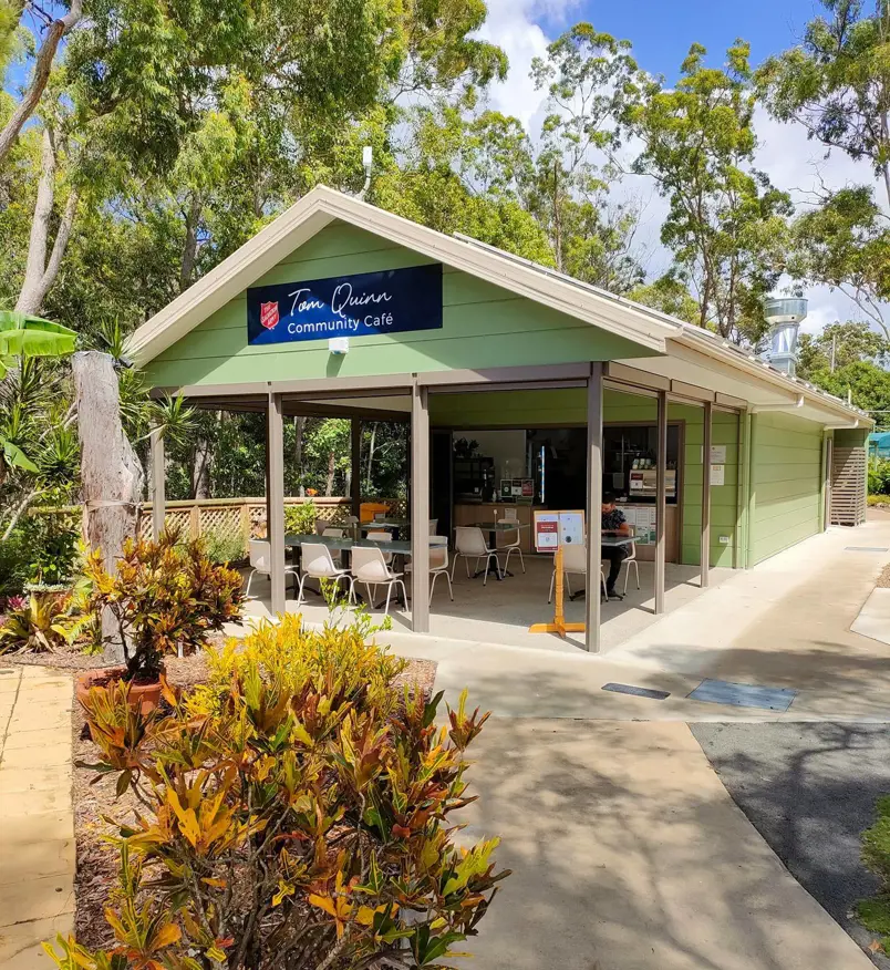The Tom Quinn Community Cafe - a light green, pitch-roofed cabin with a shaded outdoor area
